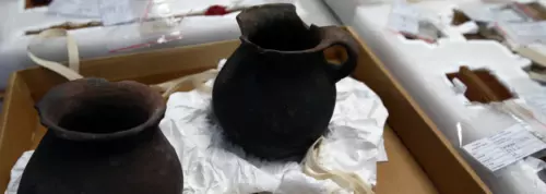 Two ancient black pottery vessels on display, one prominently featuring a handle.